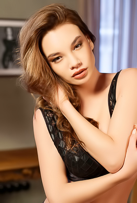 Clara poses nude and topless in black lingerie, teasing in a plush armchair with her curly hair framing her curves